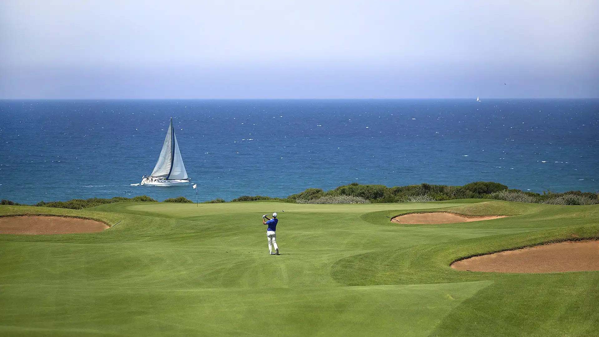 Golfer on The Dunes course with a yacht on the sea behind