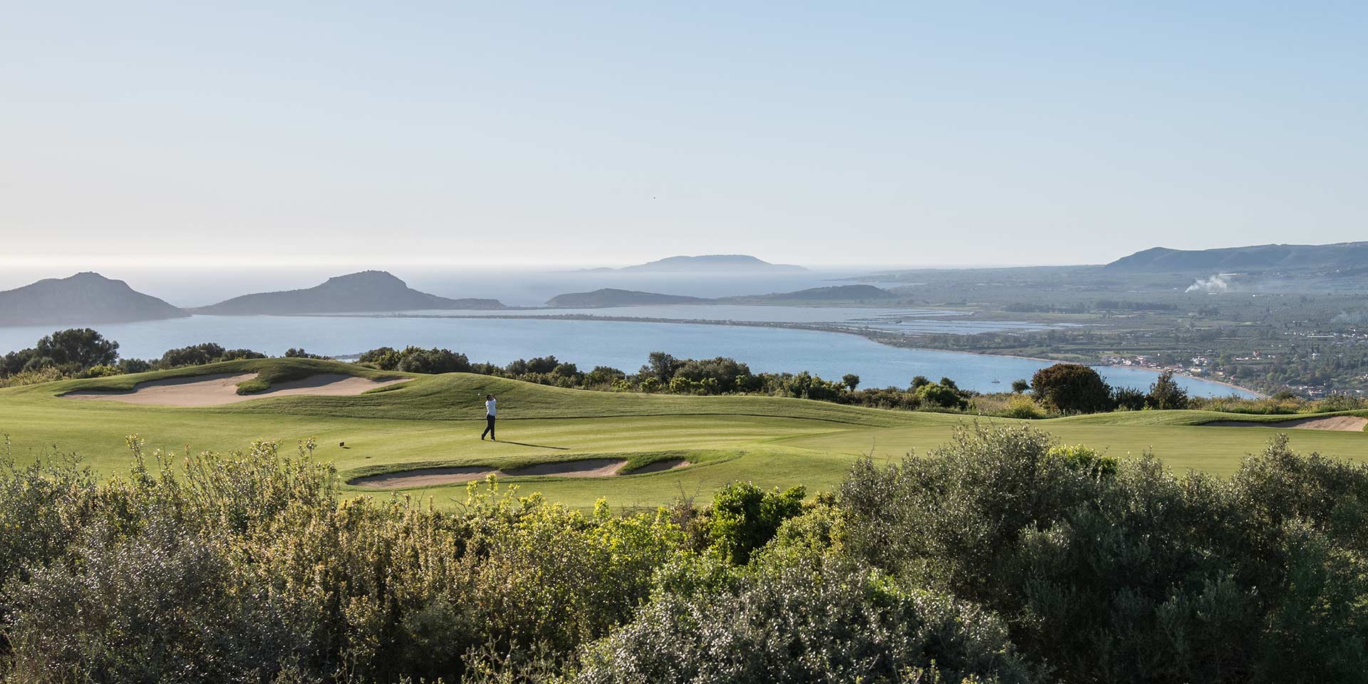 Golfer teeing off above Navarino Bay at Costa Navarino
